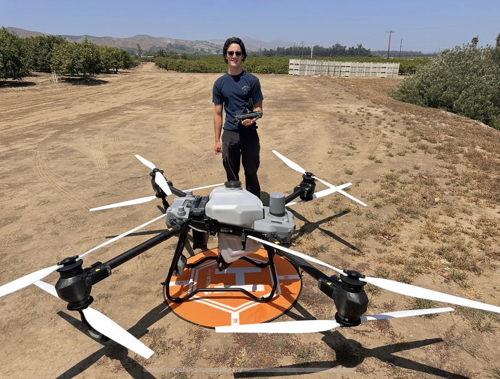 Operator standing with an agricultural application drone in an orchard